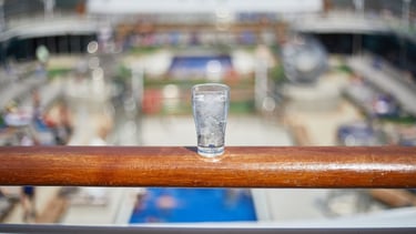 Copo de água sobre o deck do navio com vista para o mar, destacando bebidas e segurança a bordo
