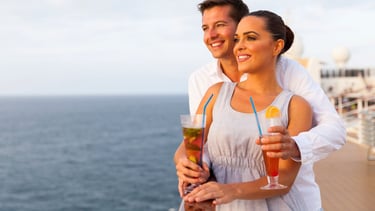 Casal apreciando drinks no deck do navio com vista para o mar, representando pacote individual e consumo por pessoa
