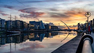 Docklands em Dublin ao pôr do sol, com reflexos dourados sobre o rio Liffey.