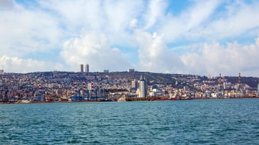 Navio chegando ao porto de Haifa visto do convés, com a cidade se estendendo ao pé do Monte Carmelo.