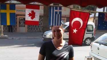 Foto da autora no centro de Izmir, entre uma bandeira turca e a movimentação local.