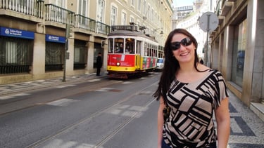 Foto da autora no centro de Lisboa em frente ao Elétrico 28 passando ao fundo
