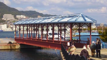Ponte sobre a marina de Nagasaki, com barcos ancorados e colinas da cidade ao fundo.