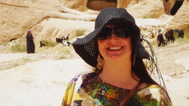 Autora saindo de Petra, com uma família beduína ao fundo, em meio às formações rochosas e ao cenário