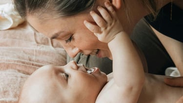 baby lying on his back, staring up at his mom's face smiling