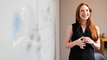 a woman in a black top and jeans standing in front of a white board