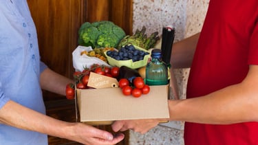 a man and woman holding a box of fruit and vegetables