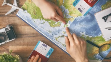 Hands pointing at a world map with travel accessories like a camera, passport, and boarding pass for vacation planning.