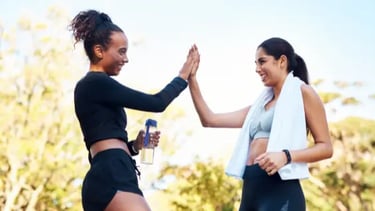 Two smiling women in workout gear giving a high five after an outdoor fitness session.