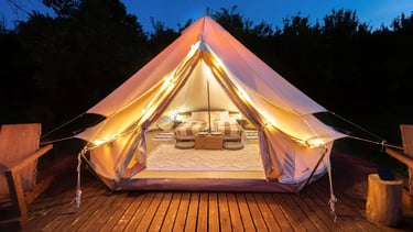 Luxury glamping bell tent at night with warm string lights, cozy interior bed, and wooden deck.