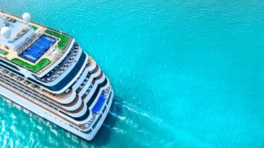Aerial view of a luxury cruise ship sailing on vibrant turquoise ocean water during a tropical vacation.