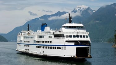 A large BC Ferries vessel sailing through scenic mountain fjords on the Pacific coast.