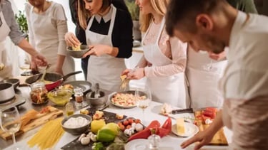 A diverse group of people wearing white aprons during a hands-on Italian cooking class.