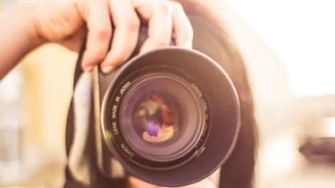 A photographer holding a professional DSLR camera lens with sunlight flare during an outdoor photoshoot.