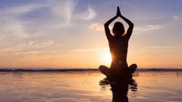 Silhouette of a woman practicing yoga in a seated lotus pose on a beach at sunset.