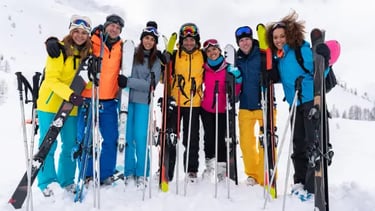 A group of diverse friends smiling on a snowy mountain with their skiing and snowboarding gear.