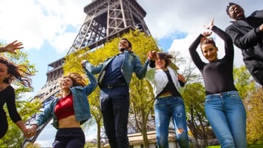 A diverse group of happy friends jumping and holding hands in front of the Eiffel Tower in Paris.