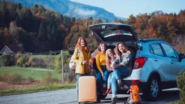 A happy family with luggage poses by their SUV during an autumn mountain road trip.