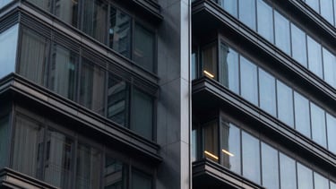 Close-up architectural photography of a modern building's facade, showing a blend of steel and glass in a Latin American urban setting, sophisticated evening lighting with colors of dark slate and blue grey, professional and sharp composition.