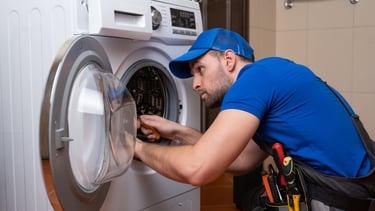 a man in a blue shirt is fixing a washing machine