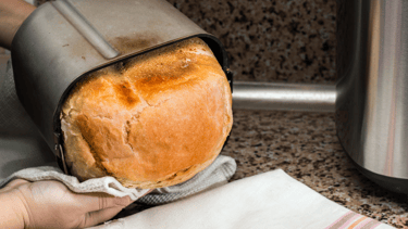 a person holding a loafed bread in a kitchen
