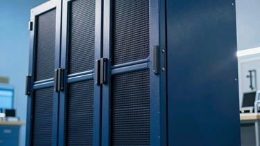 Industrial photography of a sleek, dark blue mainframe unit within a high-security North American facility, bathed in sharp sky blue light.