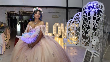 Quinceañera feliz en su fiesta con vestido rosa y ramo iluminado, rodeada de una hermosa decoración.