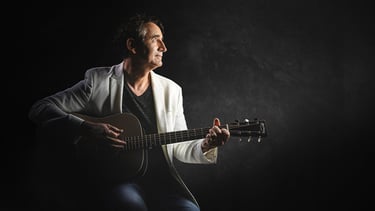 Joël Royer en photo avec sa guitare et de profil avec un fond noir