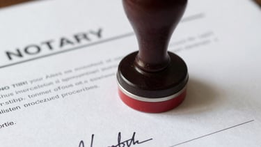 A mobile key duplication cart is situated on a street, featuring a sign with bold red lettering on a bright yellow background. The cart is equipped with wheels, allowing it to be easily moved. The surrounding area includes a sidewalk and buildings with various colors and architectural details. A person is riding a motorcycle in the background.