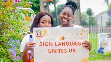 2 women smiling while holding a banner that says "Sign language unites us"