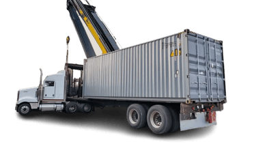 A heavy-duty reach stacker crane loading a grey metal shipping container onto a white semi-truck trailer.