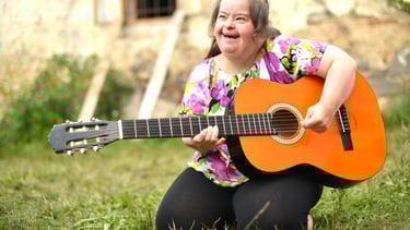 Photo of a young lady with special needs playing a guitar outside