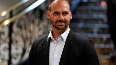  Eduardo Bolsonaro de terno, com barba, olhando para o lado e sorrindo levemente.
