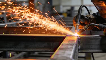 A professional welder in safety gear uses a torch to weld steel beams, creating bright orange sparks.