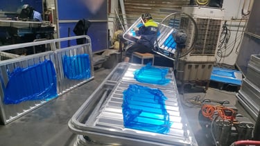 Professional welders fabricating aluminum frames in an industrial metal manufacturing workshop.
