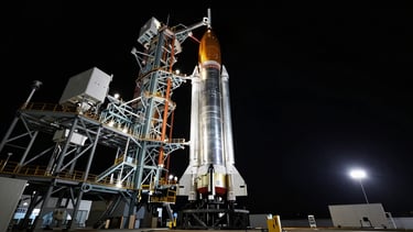 Wide-angle cinematic capture of a massive stainless steel rocket booster on the launchpad at dusk, dramatic cold rim lighting, deep black sky.