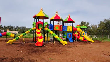 A large colorful outdoor playground equipment set with slides, tunnels, and climbing towers on a red dirt surface.