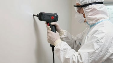 A focused wide shot of a professional mold remediation technician in a North American / US / Florida home, wearing a protective white suit and safety gear, efficiently using a specialized moisture detection scanner on a drywalled corner. The lighting is bright and industrial, emphasizing clarity and precision, with subtle dark gray and red equipment accents to convey urgency and high-tech expertise.