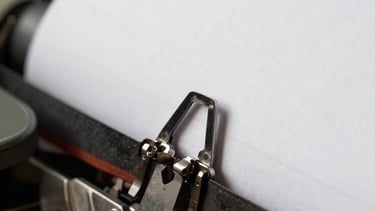 Close up photograph of a vintage silver typewriter hammer striking white paper, creating a sharp bone white and charcoal gray contrast, North American / US style.