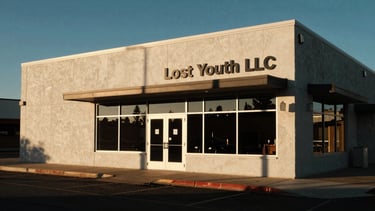 High-contrast architectural shot of the Lost Youth LLC studio exterior in Pocatello, Idaho, at golden hour, harsh shadows, warm amber accents, wide environmental shot.