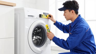 Medium shot of a professional technician in a clean uniform using a level on a newly installed premium washing machine, bright daylight.