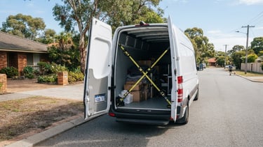 A clean white transport van parked on a sunny Perth suburban street, secure straps visible through the open back door, bright Australian daylight.
