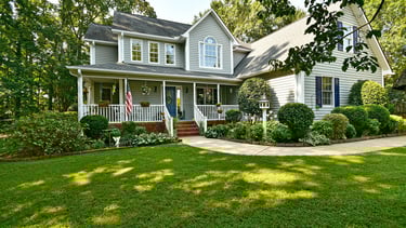 Two-story grey traditional home with white trim, a large front porch, and lush green lawn.