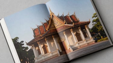 Top-down view of a spread in an art book showing large, clear photos of Southeast Asian architecture. The paper is heavy and matte. Soft afternoon shadows.