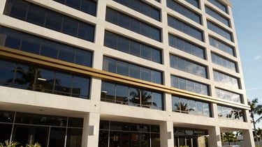 Wide architectural shot of a modern, sunlit office building exterior in Hobe Sound, Florida, with clean lines and large windows, natural coastal daylight, deep navy and warm gold accents, 35mm lens.