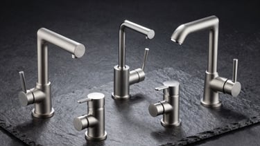 Sleek commercial-grade stainless steel wash basin mixers and shower fixtures arranged on a dark slate background.