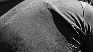 Stark monochrome macro shot of textured cycling speed fabric, high-contrast direct sunlight, deep shadows, sharp technical details, 35mm film grain