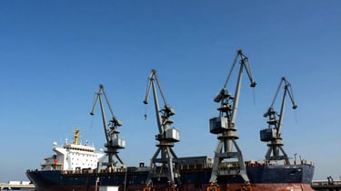 Wide-angle architectural photograph of a modern industrial marine shipyard in Karachi, towering steel cranes, high-contrast daylight, deep blue sky, metallic steel tones.