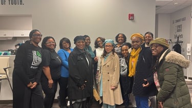 A group of smiling women posing for a community photo in a bright indoor office setting.