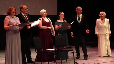 A group of diverse singers in formal attire performing a choral concert on a theater stage.